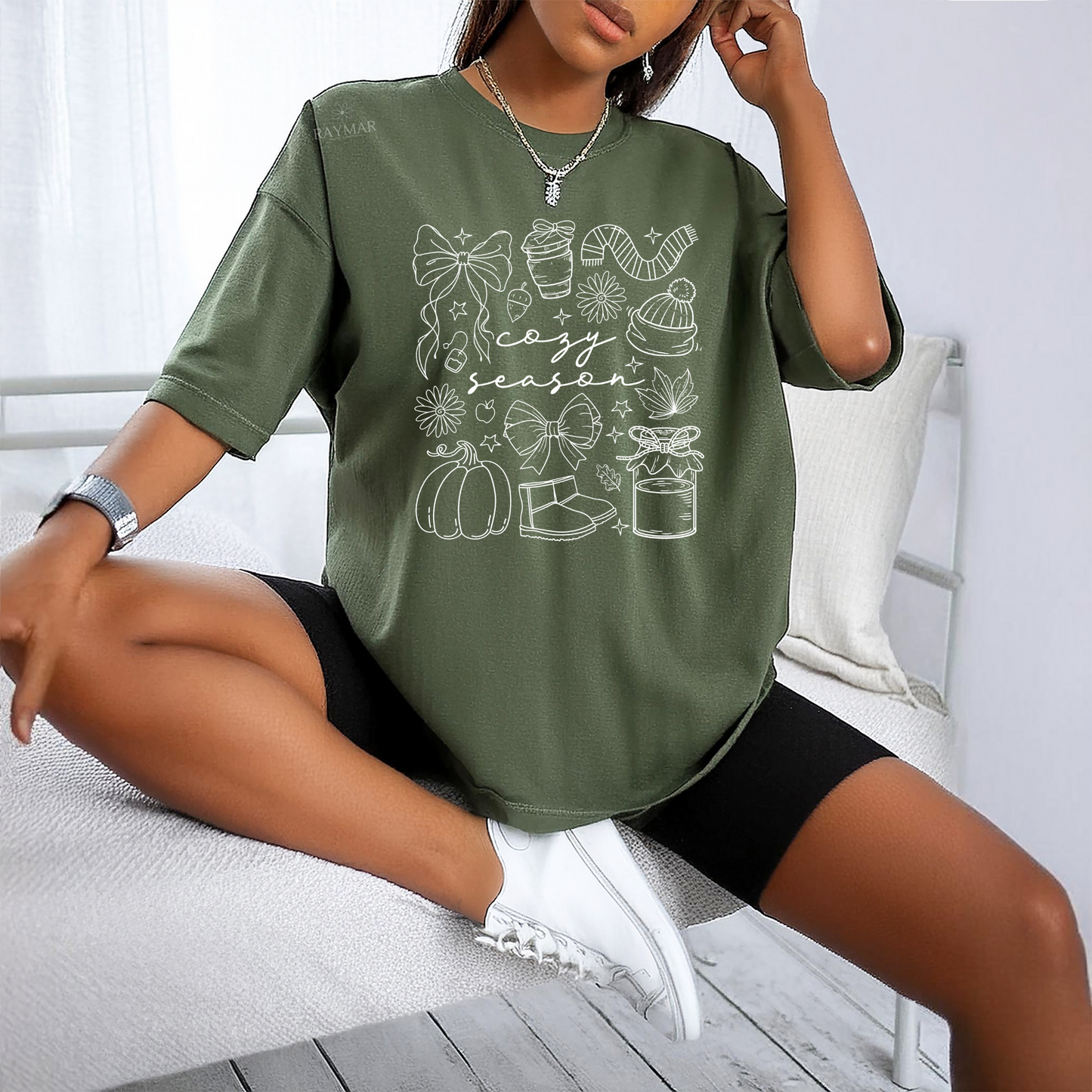 Person wearing a green t-shirt with a 'cozy season' design sitting on a white bench.
