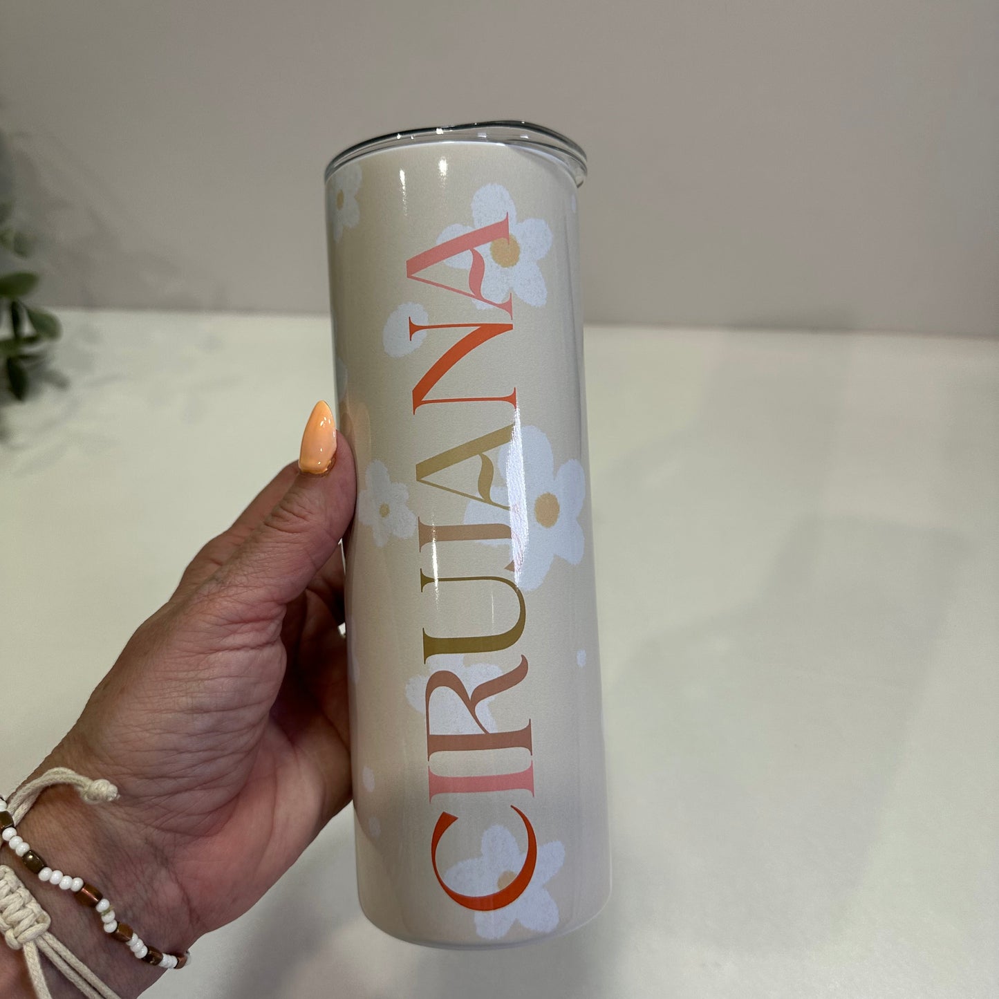Hand holding a Cirujana bottle against a neutral daisy flowers background