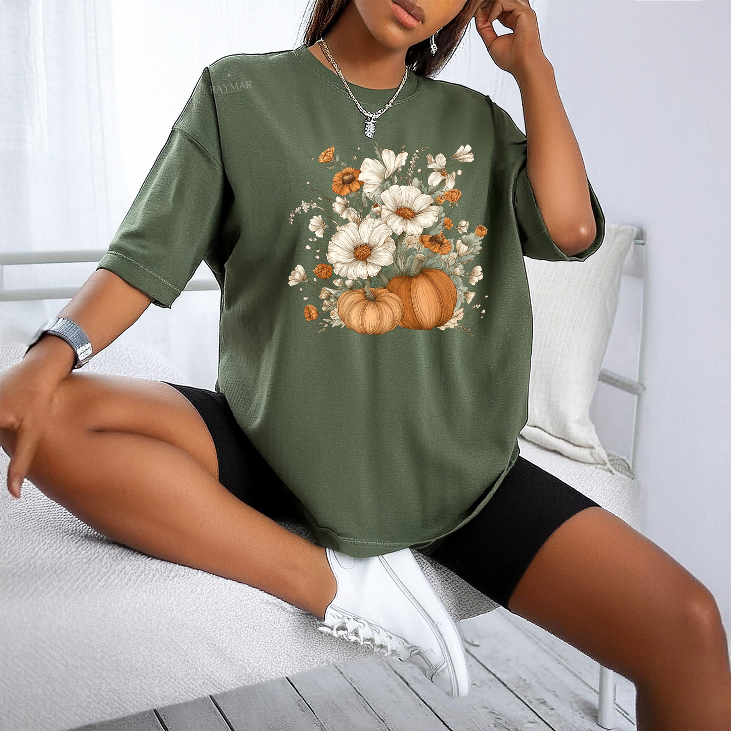 Person wearing a green t-shirt with floral and pumpkin design, sitting on a white bench.