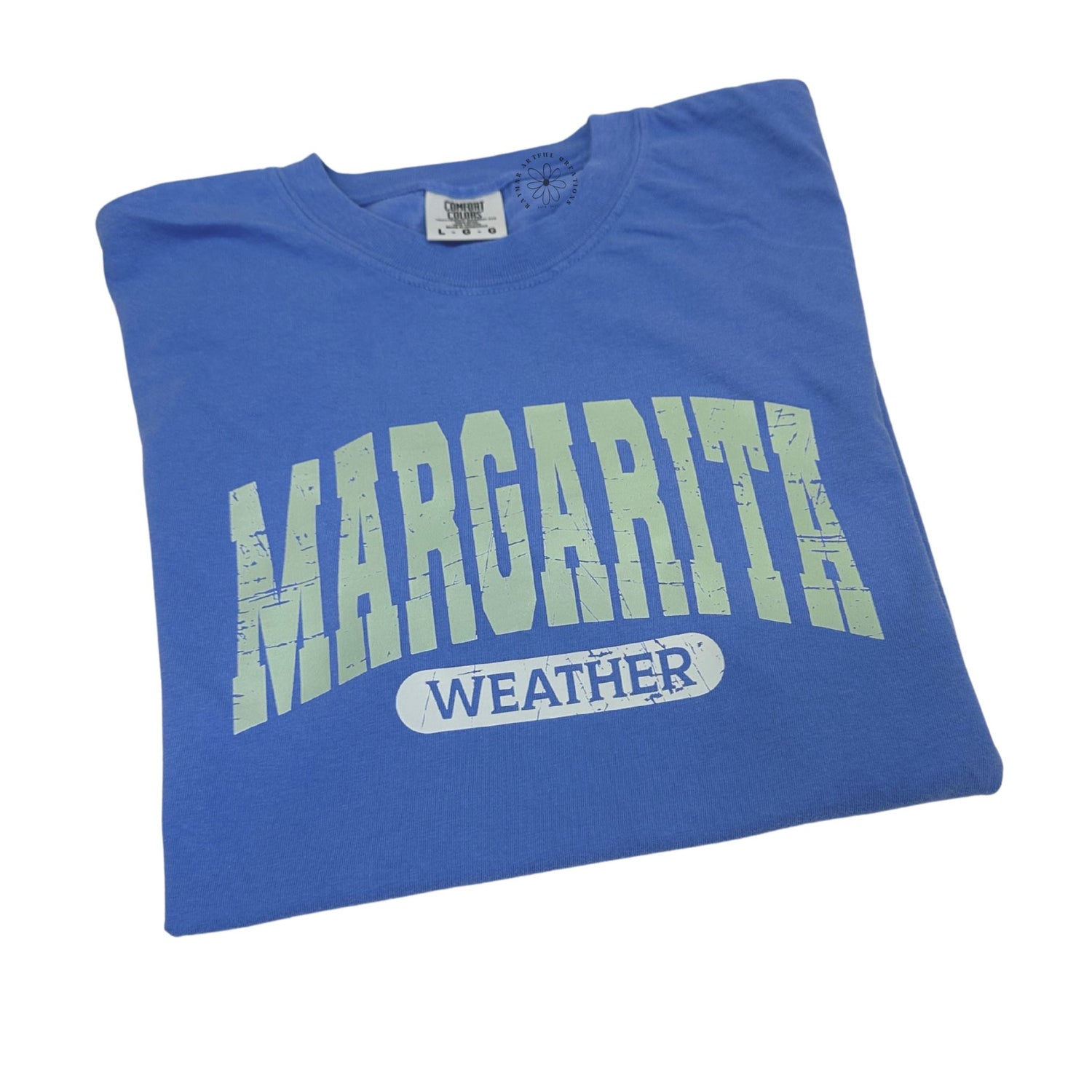 Folded blue t-shirt with 'Margarita Weather' text on a white background