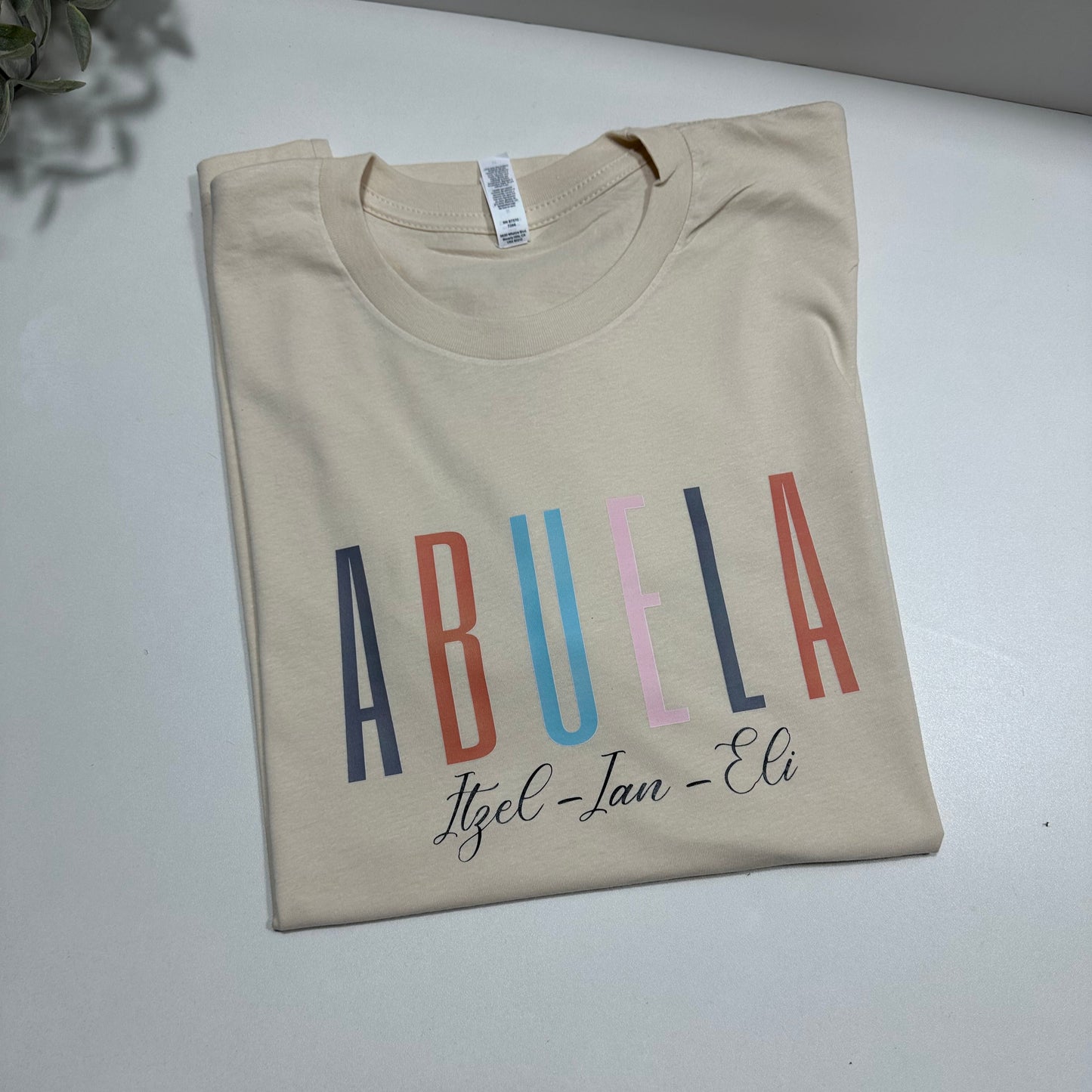 tan shirt with abuela graphic design , each letter is different color and has the kids names in black color under abuela