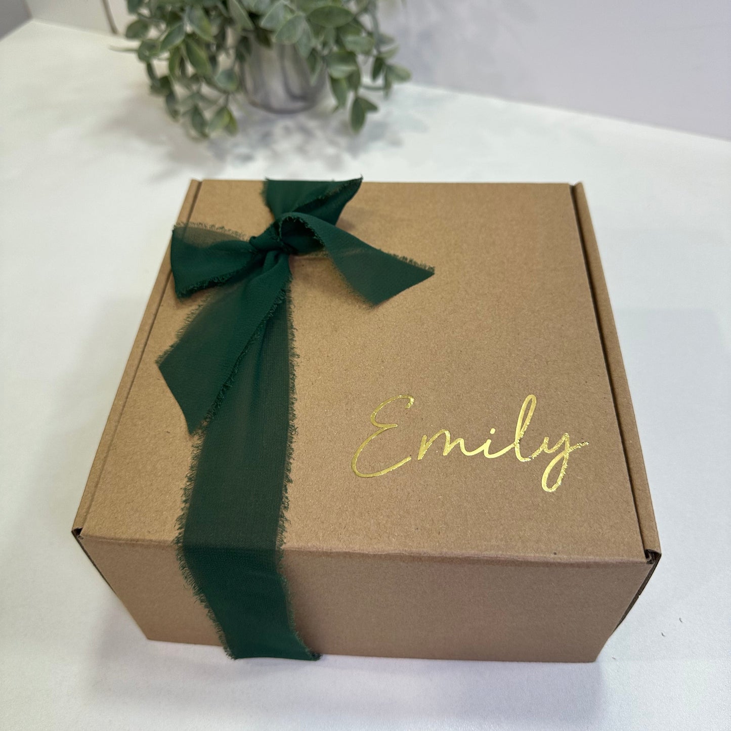 kraft box with name in gold and a dark green bow