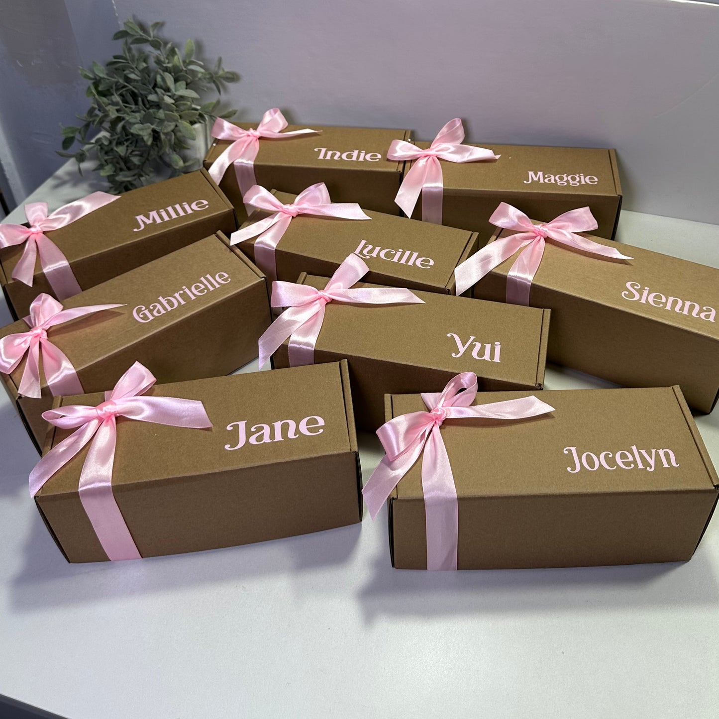 Brown gift boxes with pink ribbons and names on a white wall.