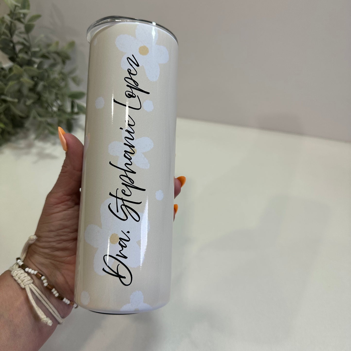 Hand holding a cylindrical tumbler with floral designs and text against a neutral background