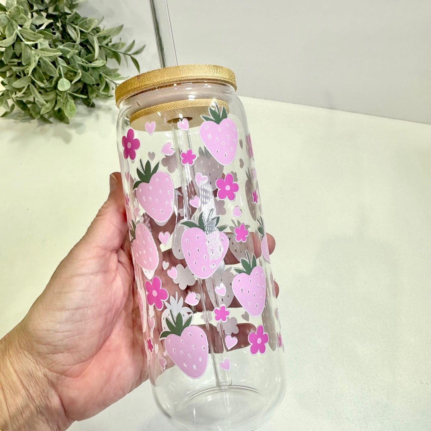 Light Pink Strawberry tumbler with floral and hearts design held by a hand, against a light background.