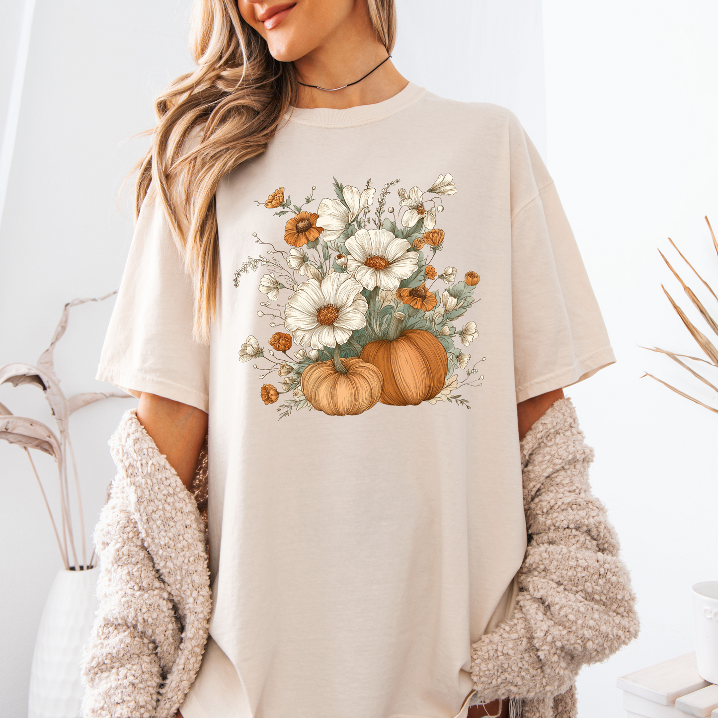 Person wearing a beige t-shirt with a floral and pumpkin design.