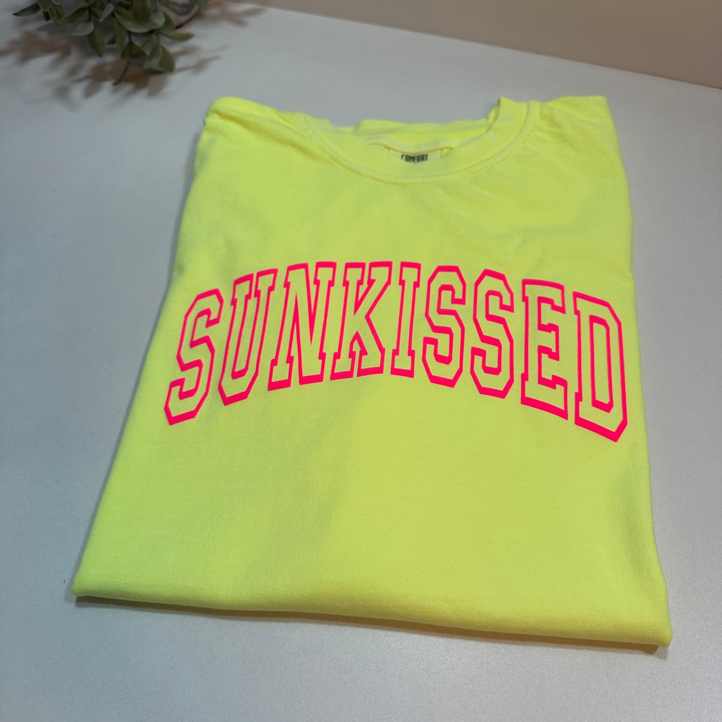 neon lemon shirt lay down with neon pink Sunkissed puff design on a white background