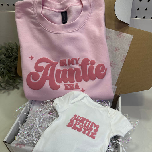 Pink sweatshirt that said in my auntie era and white onesie  with ''Auntie's Bestie' puff text in a gift box.