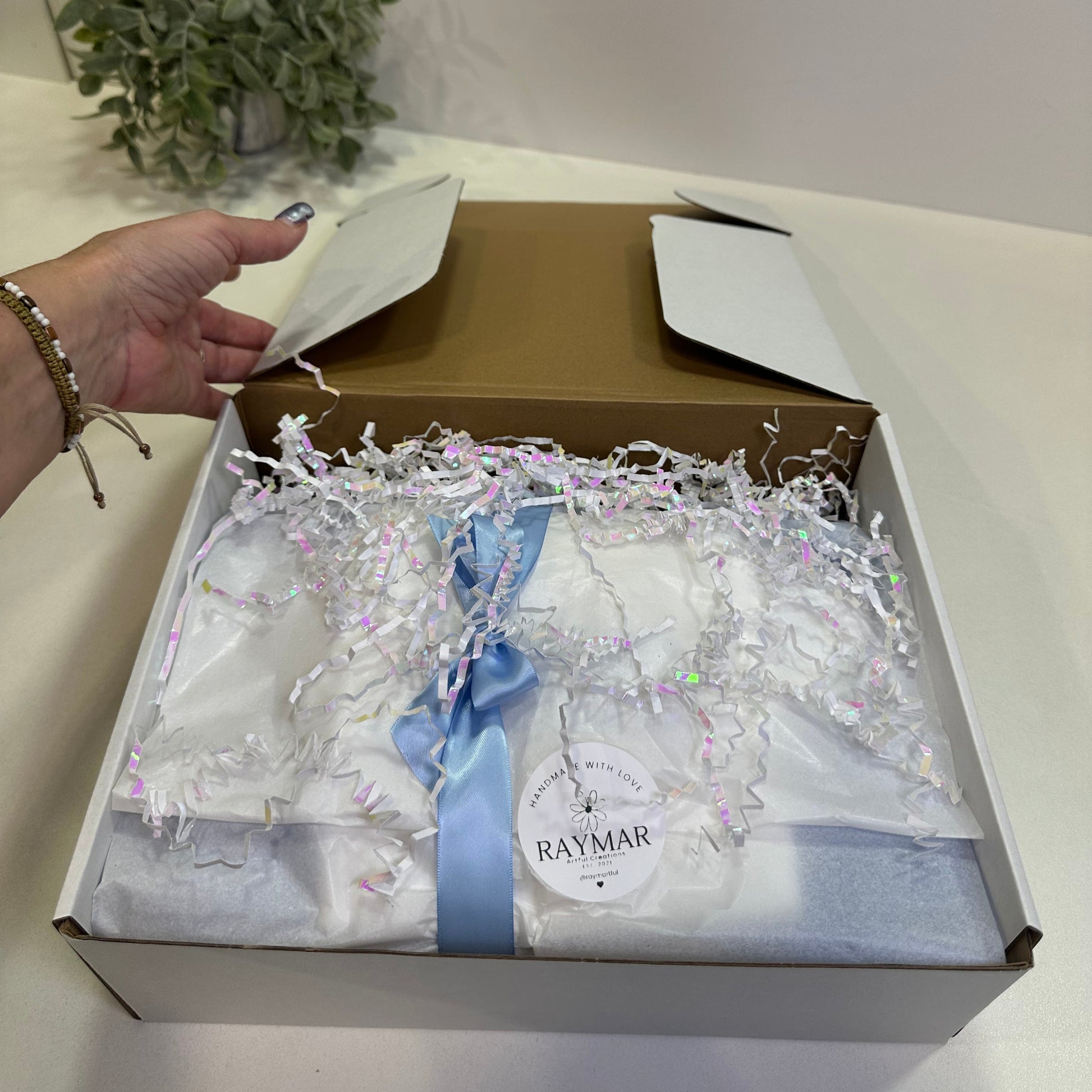 Custom Gift box with baby clothes and a bow, held by a hand against a white background