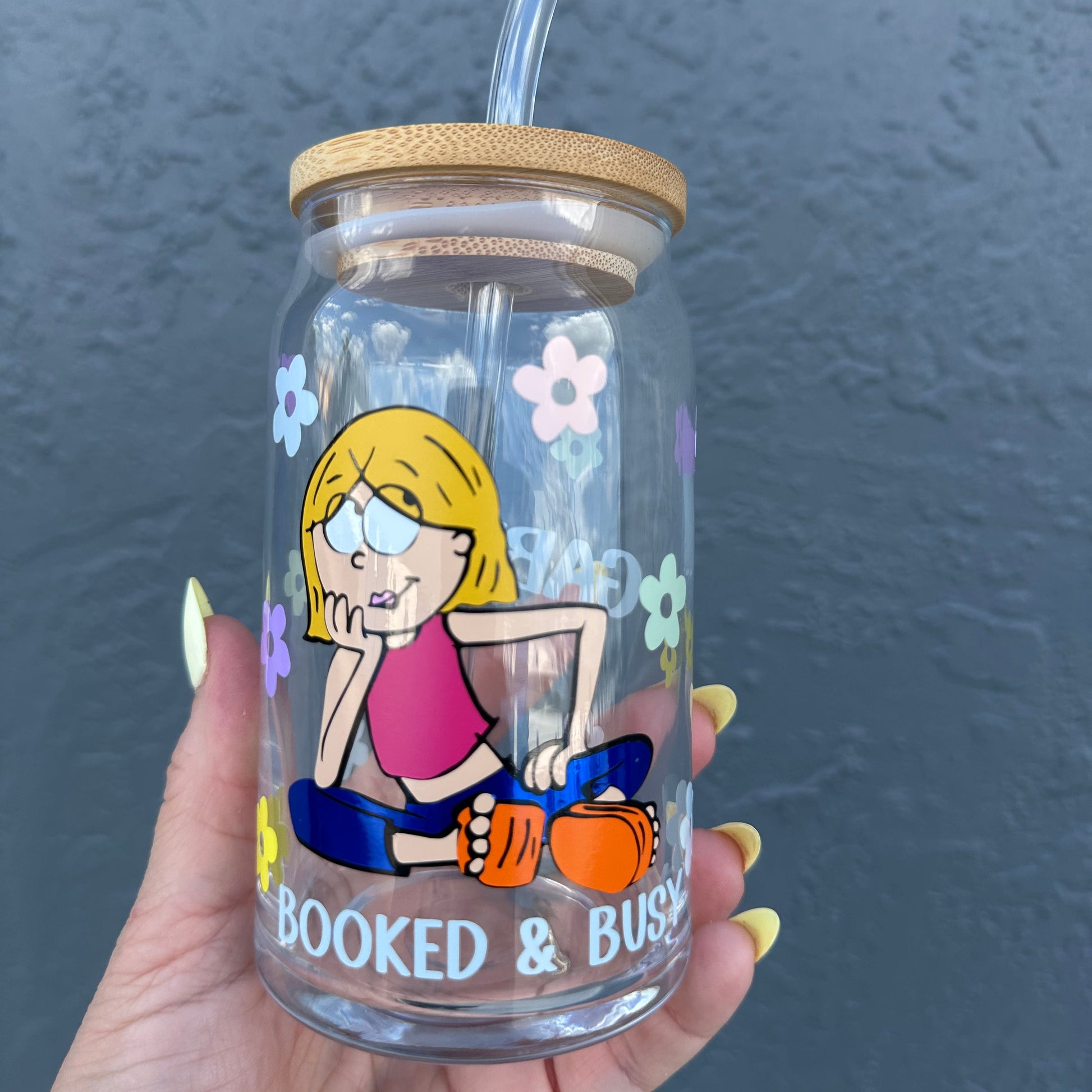 glass can cup with retro flowers daisies and lizzie McGuire seat and under a phrase that said booked and busy