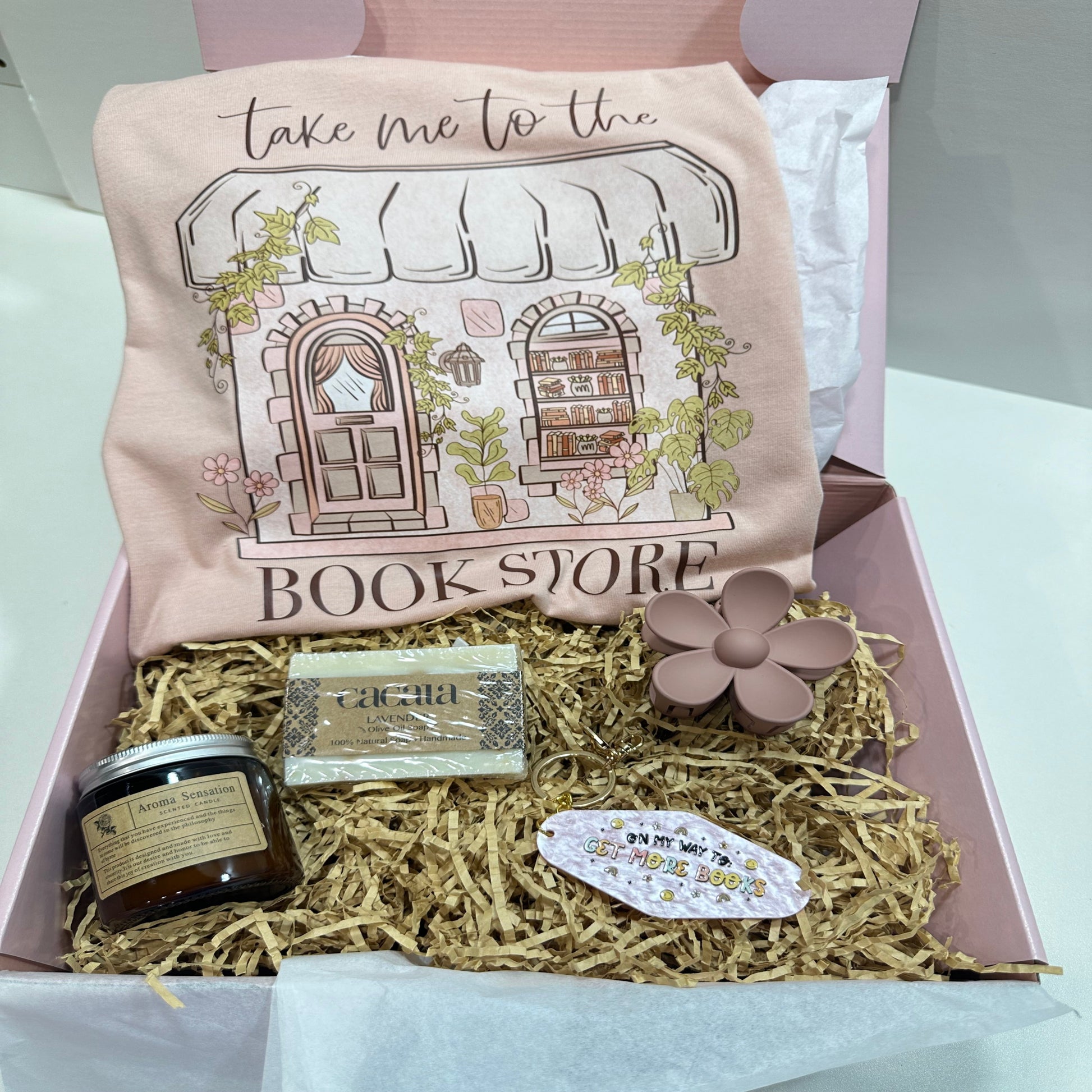 pink gift box with a take me to the bookstore peach shirt, a soap, a candle, a flower hair clip and a pink motel keychain that said on my way to get more books