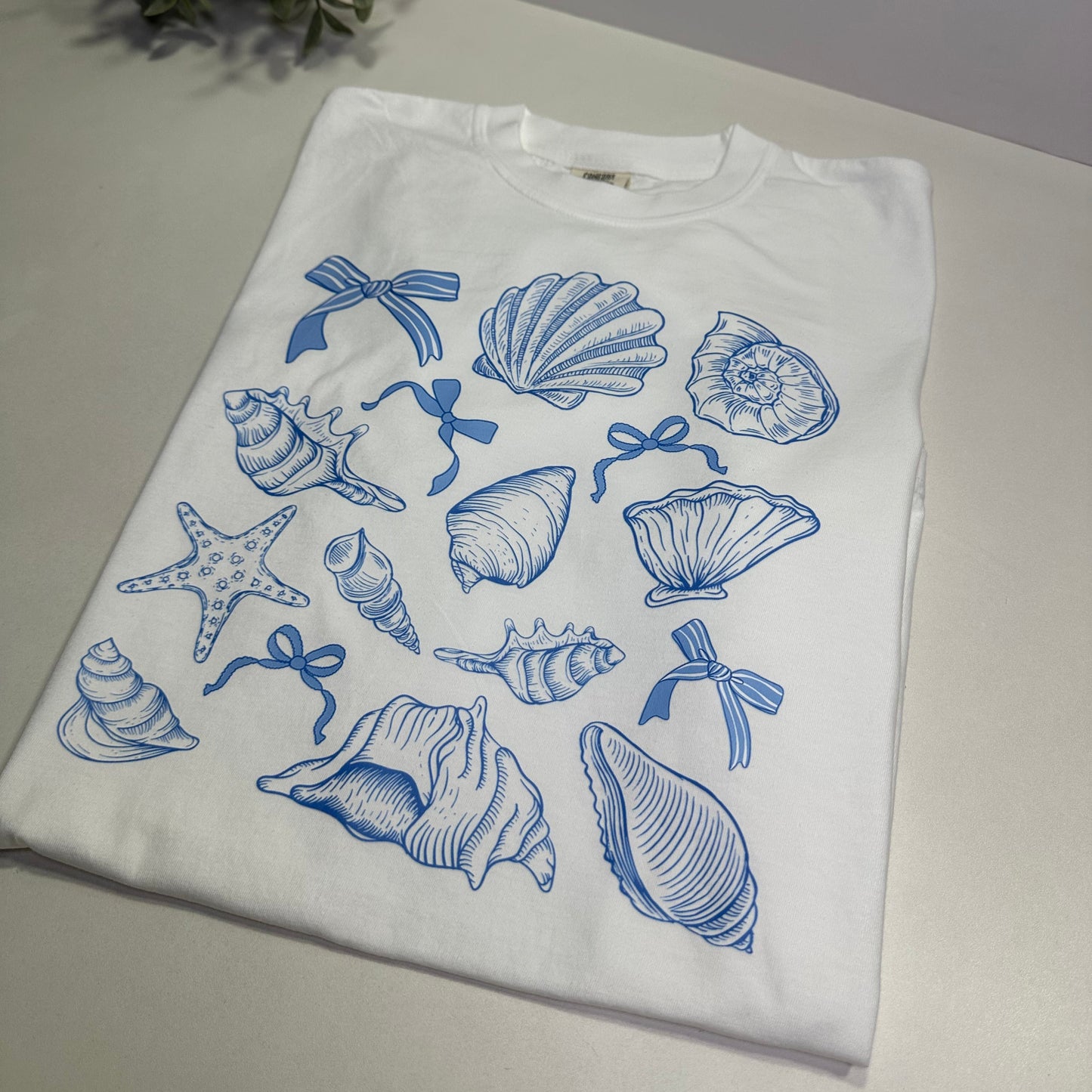 White t-shirt with blue sea-themed graphics on a white surface.