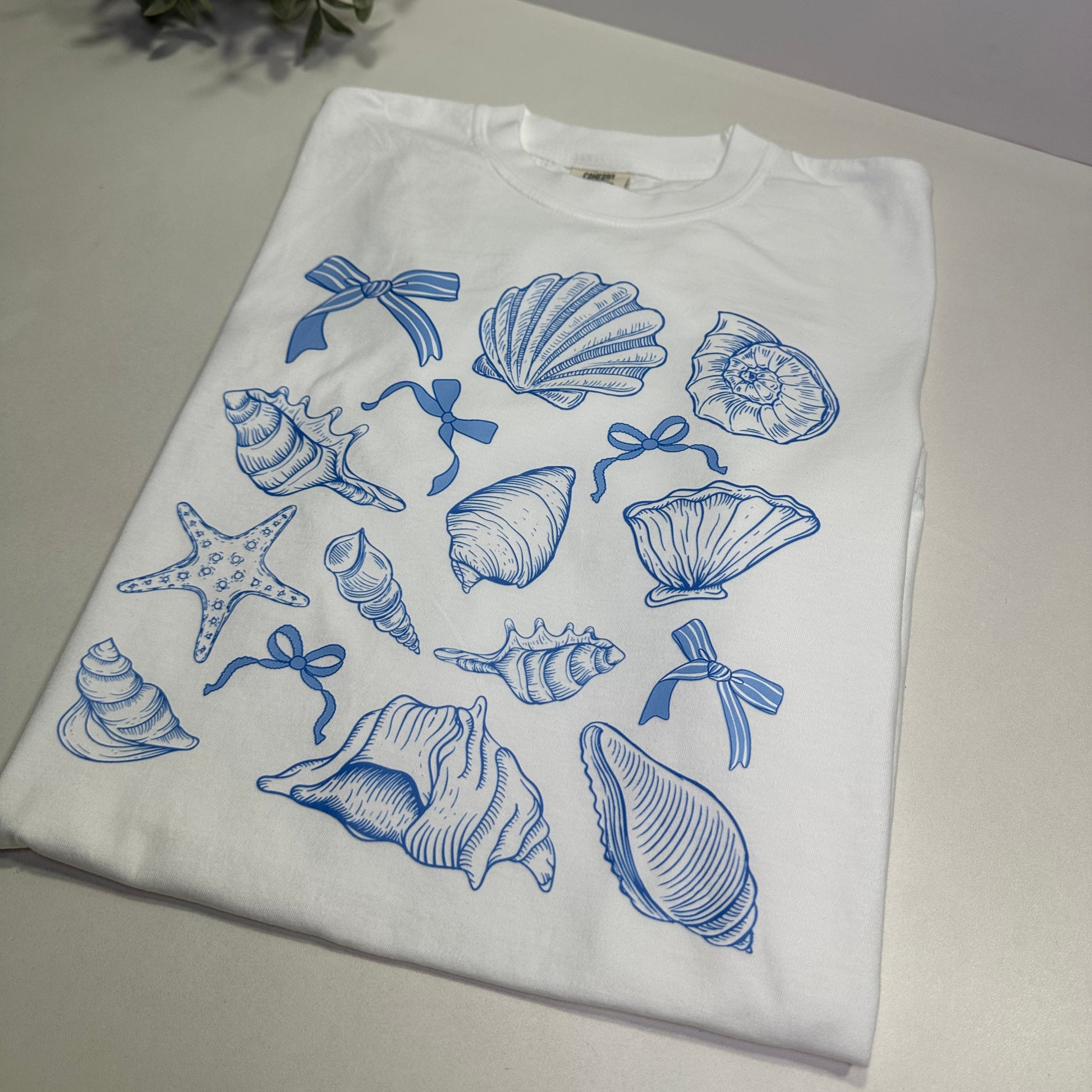 White t-shirt with blue sea-themed graphics on a white surface.
