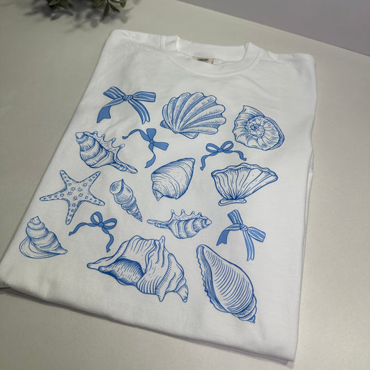 White t-shirt with blue sea-themed graphics on a white surface.