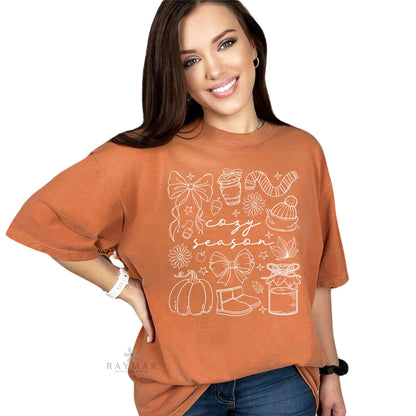 Woman wearing a rust-colored t-shirt with 'cozy season' graphic design on a white background