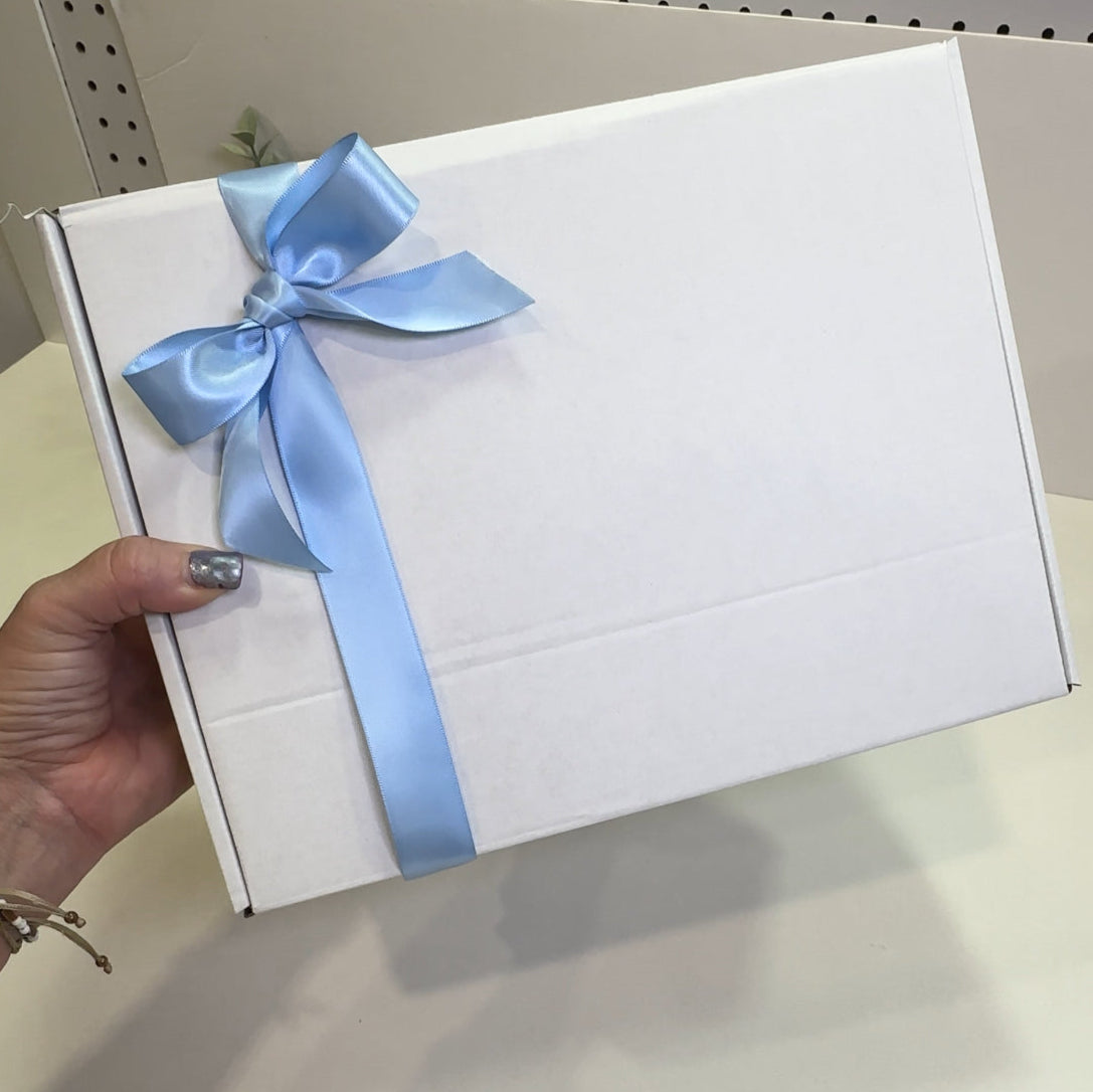 White gift box with a blue ribbon held by a hand on a light surface.