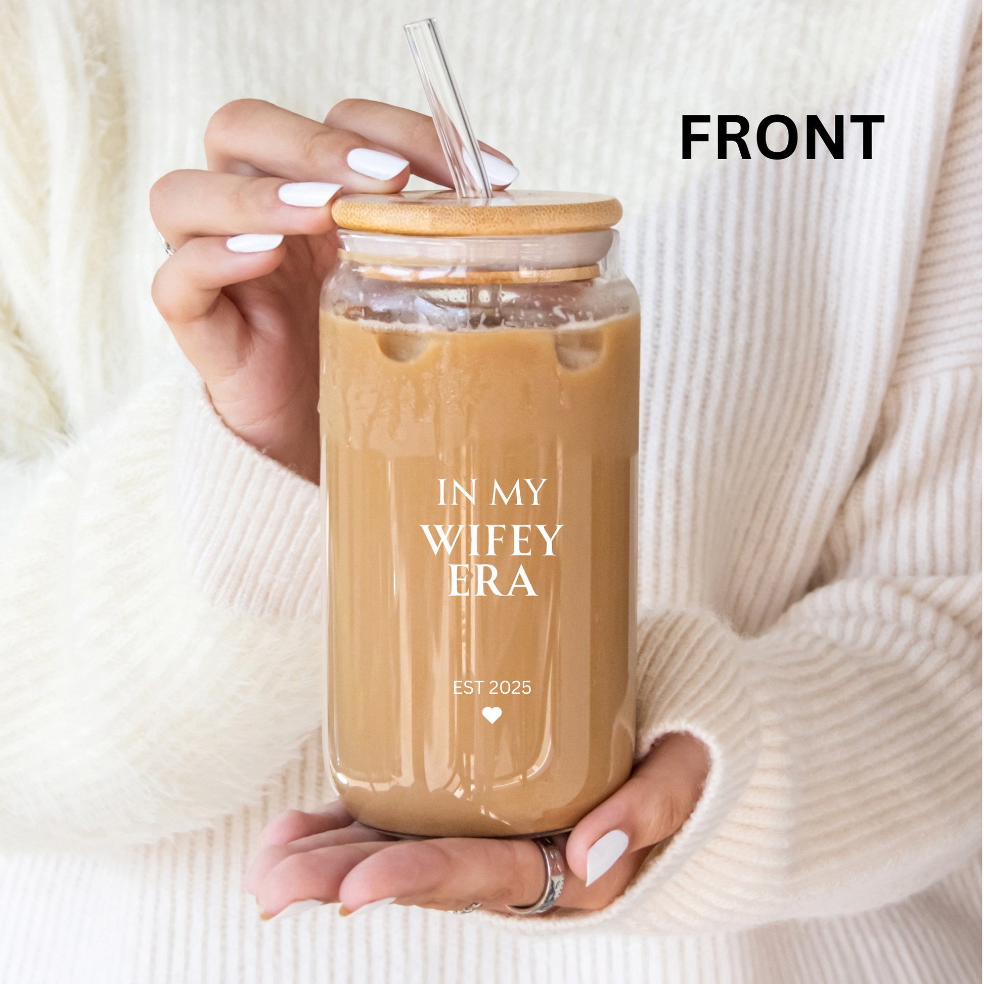 Hand holding a glass of iced coffee with a straw, labeled 'IN MY WIFEY ERA EST 2025', against a white background.