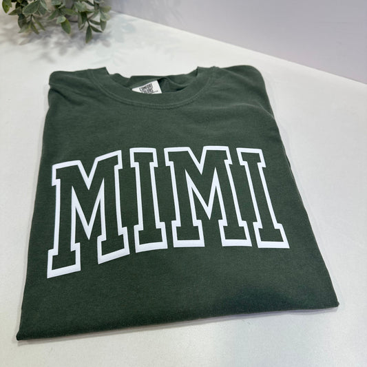 Green t-shirt with 'MIMI' printed on it, placed on a white surface.