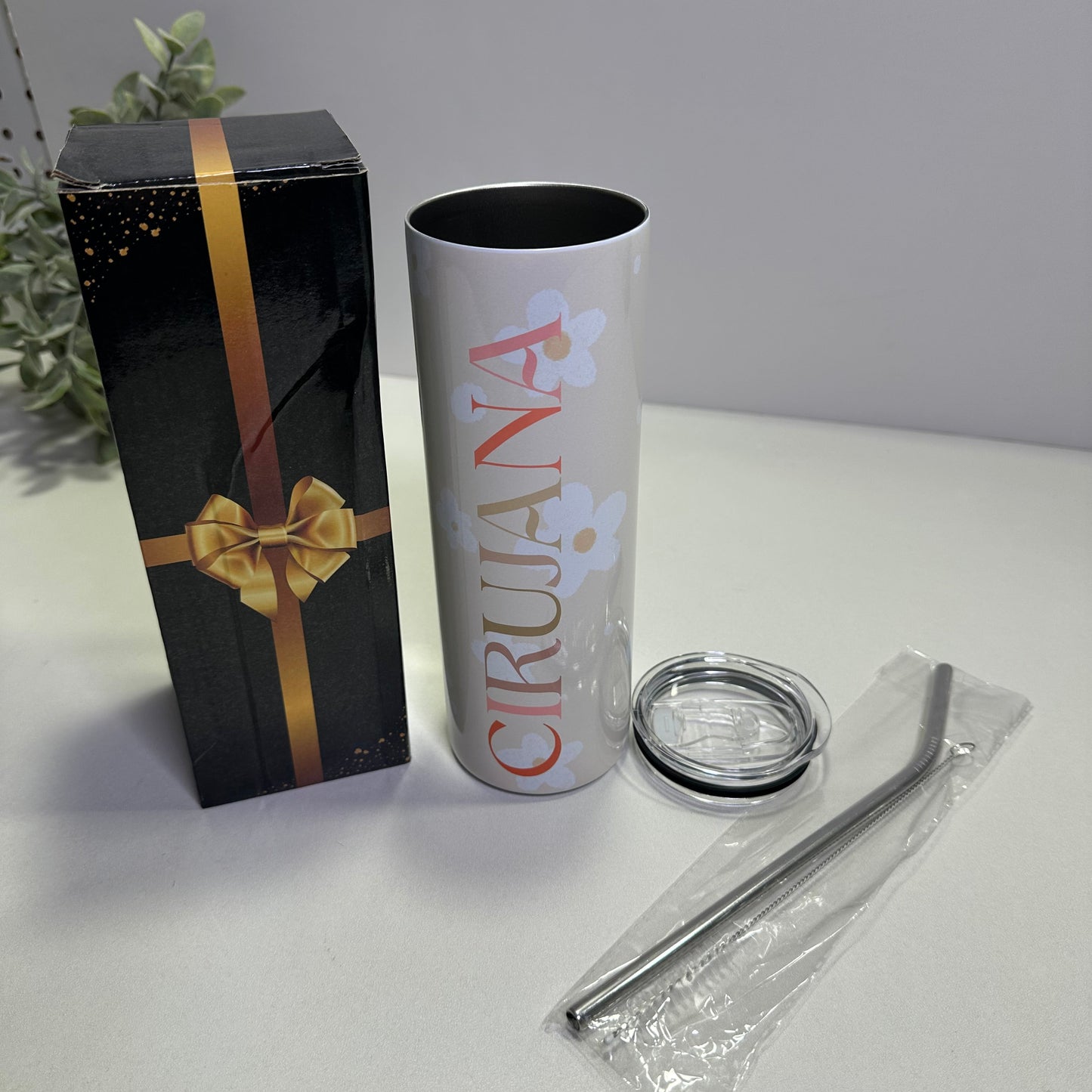 Custom tumbler product packaging with a cylindrical container, clear lid, and black box with gold ribbon on a white background.