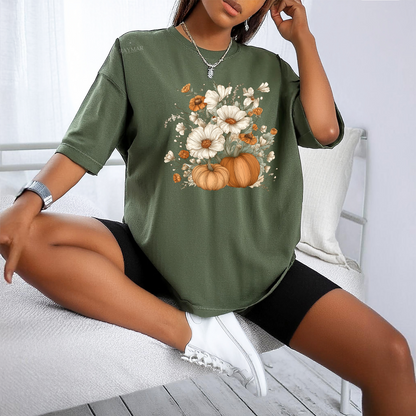 Person wearing a green t-shirt with floral and pumpkin design, sitting on a white bench.