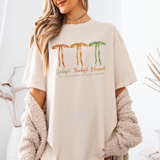 Person wearing a beige t-shirt with colorful religius text and bows fall graphics on a white background
