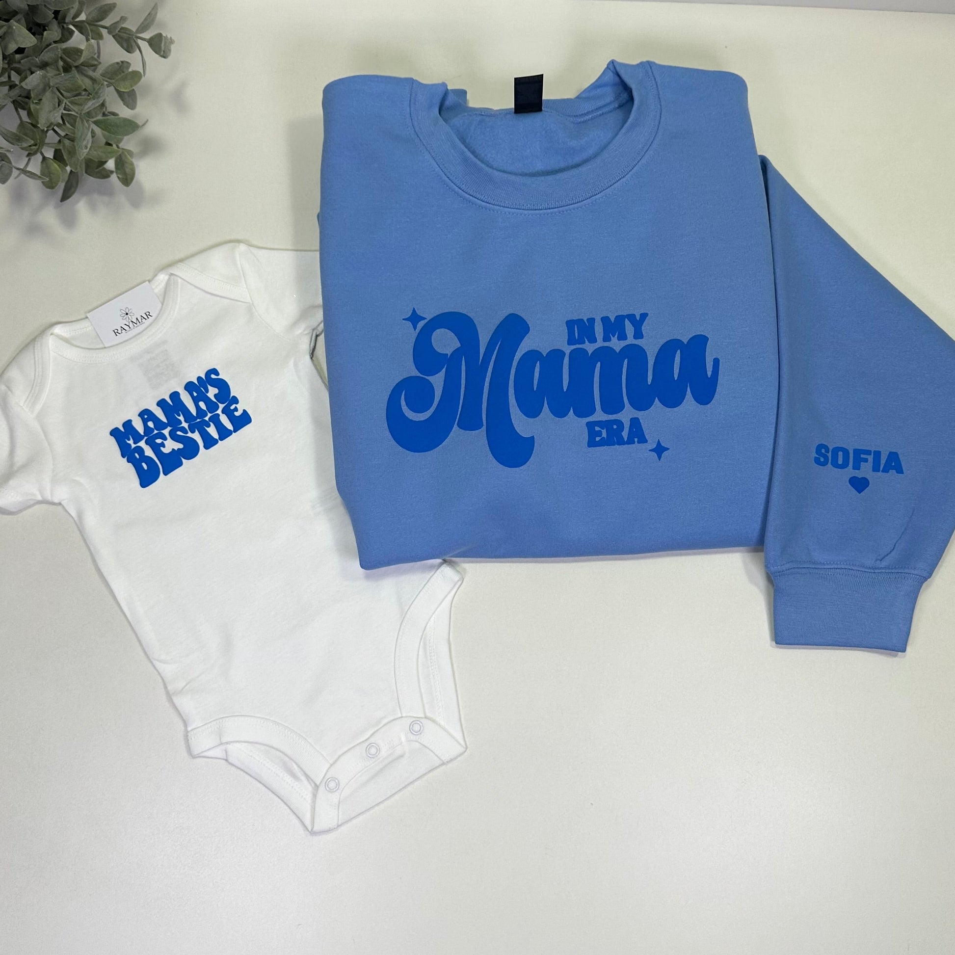Blue sweatshirt that said in my mama era and white baby onesie with text on a "mama's bestie" in blue
