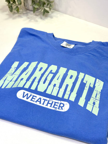 Blue t-shirt with 'Margarita Weather' text on a white surface