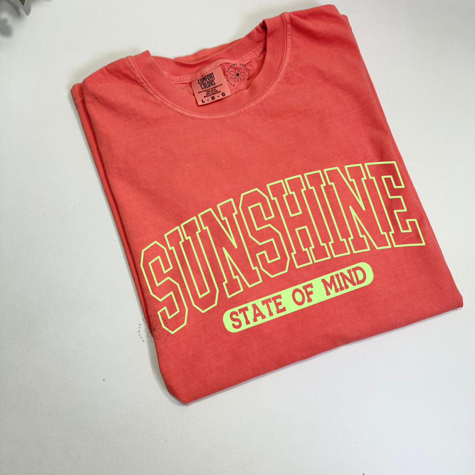 Folded neon orange t-shirt with bright yellow text "sunshine state of mind" on a white surface