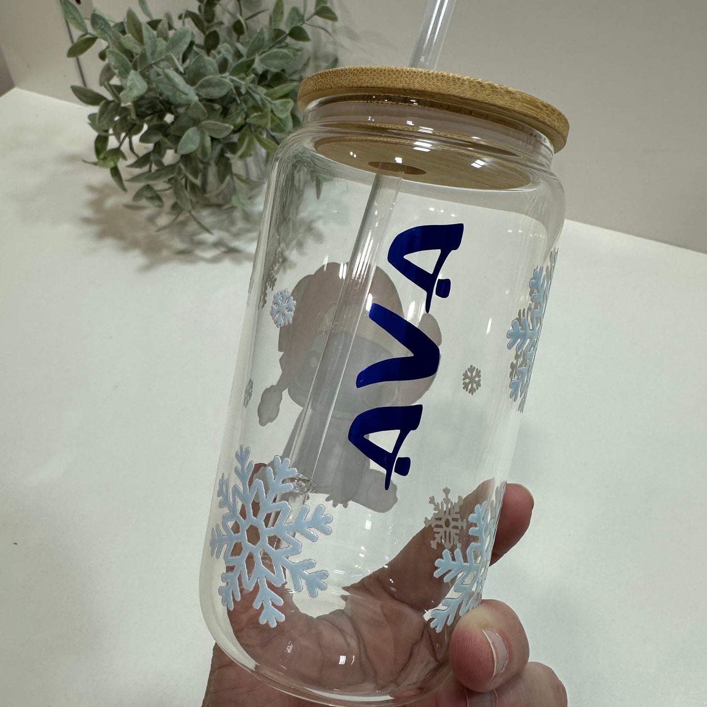Clear glass tumbler with straw and snowflake design held by a hand, with a Ava Name in blue on it