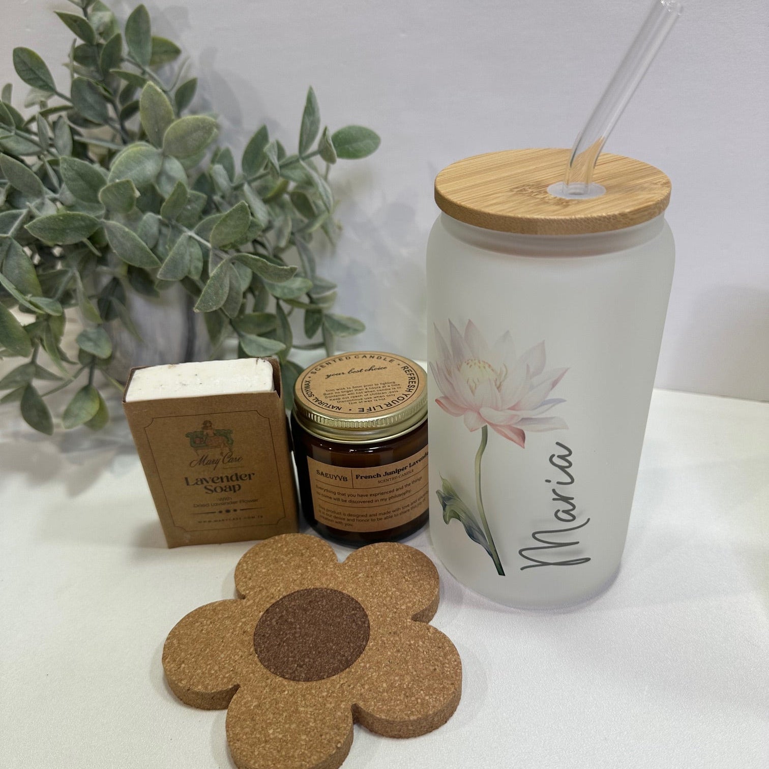 Personalized cup with flower and name with  lid and  straw. A flower coaster, soap and candle on a white surface.