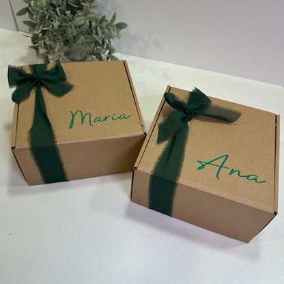 Two cardboard boxes with green ribbons and names 'Ana' and 'Maria' on a white surface.