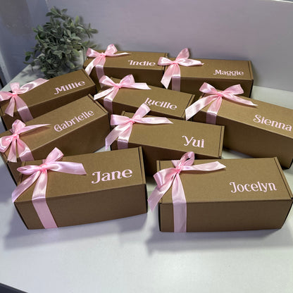 Brown gift boxes with pink ribbons and names on a white wall.