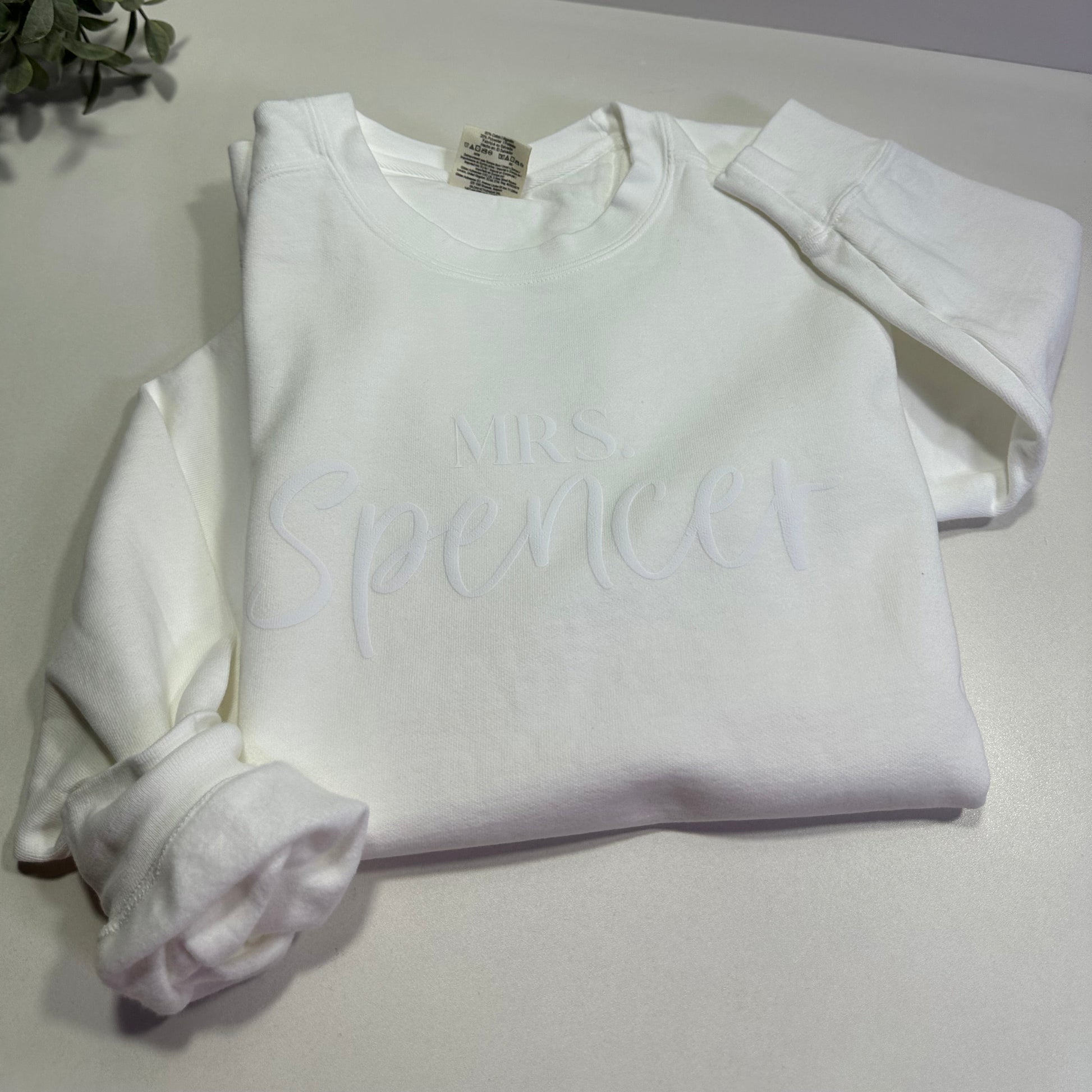 White sweatshirt with custom Mrs. design in puff  flat lay on a white table