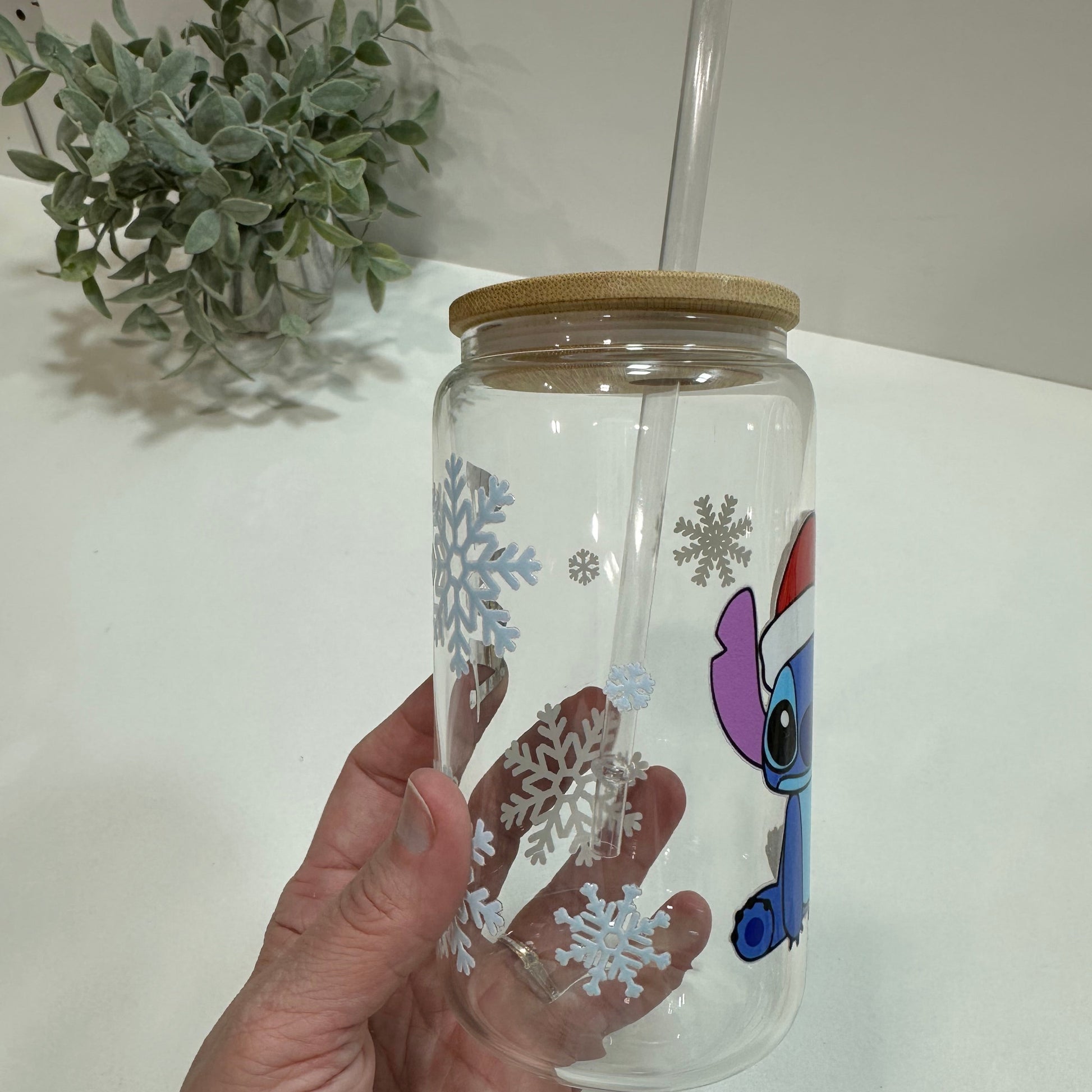 Hand holding a glass with a snowflakes design and straw lid on a white background