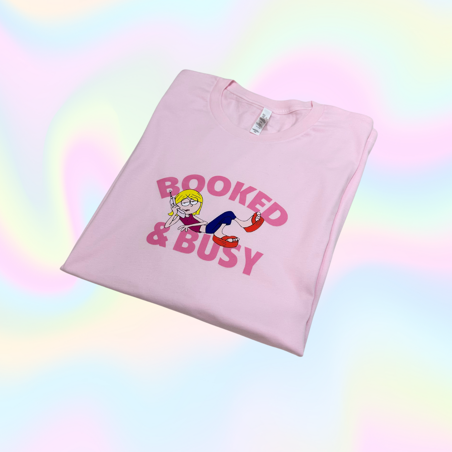light pink shirt with a graphic design booked and busy in dark pink color and Lizzie Mcguire lay down between those words with a phone