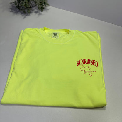 neon lemon t-shirt with orange-red text on a white surface next to a plant