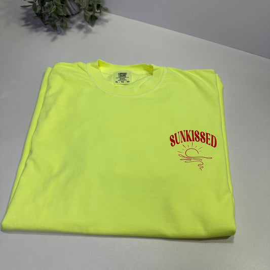 neon lemon t-shirt with orange-red text on a white surface next to a plant
