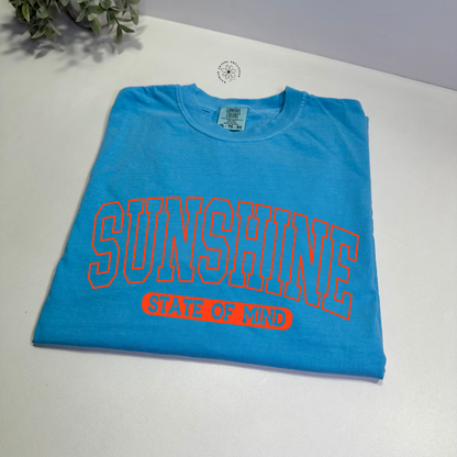 comfort colors sapphire  t-shirt with 'SUNSHINE STATE OF MIND' text on a white surface